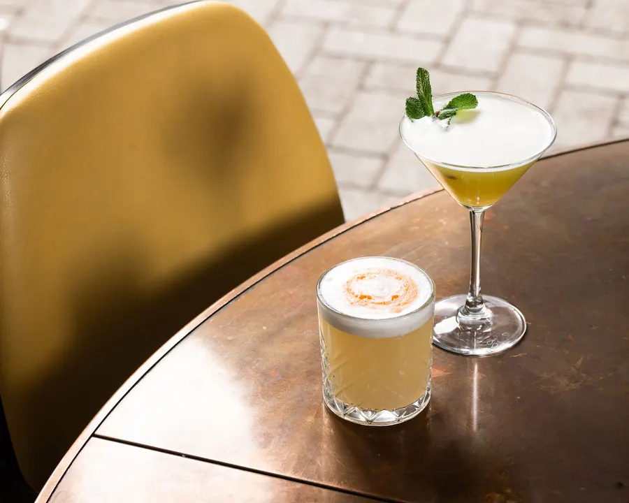 Two cocktails on a bronze table in the sun