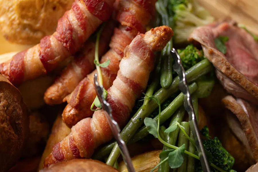 Close on a sharing roast: pigs in blankets, green beans and sliced beef