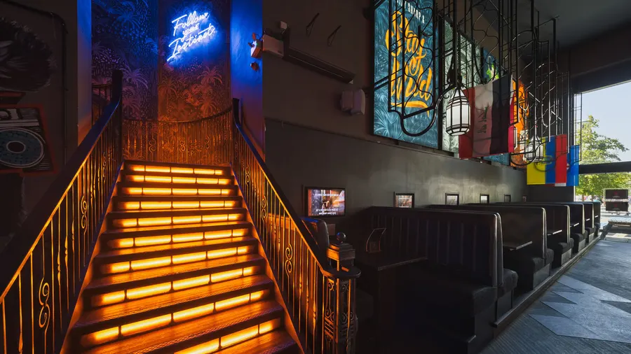 Grumpy Monkey's staircase lit orange under a blue neon sign, flags along the wall