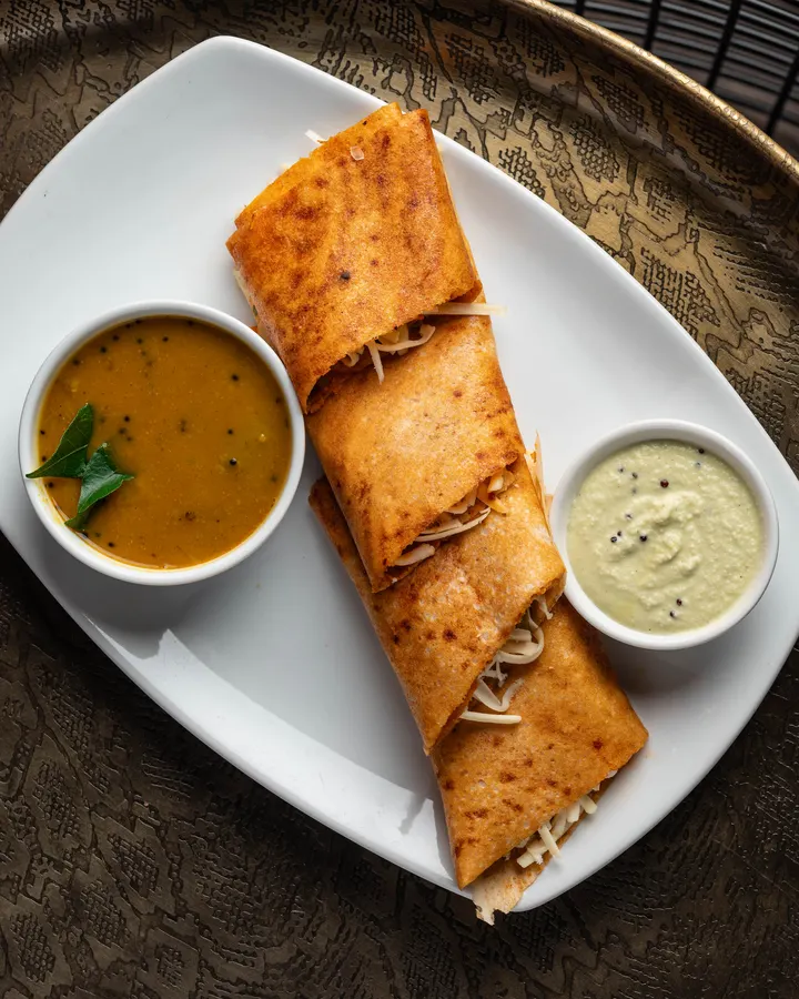 Chilli paneer dosa on a white plate with sambar and chutney