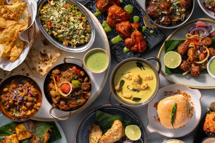 Overhead of a full Padharo table: curries, dosa, rice, breads and chutneys